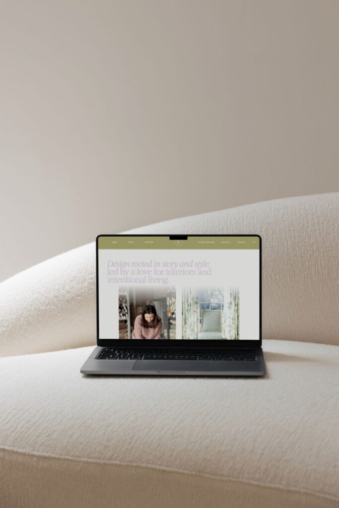 A laptop displaying a website with interior design content rests on a textured, light-colored sofa against a plain, neutral wall.