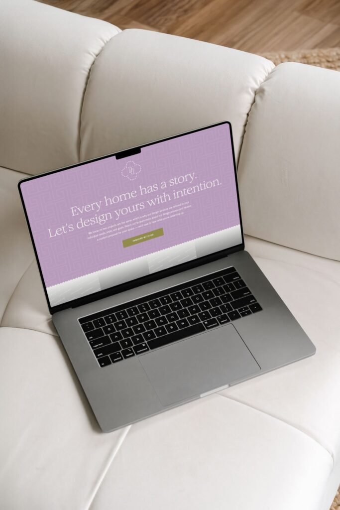 A laptop sits on a white couch, displaying a website with a lavender background and the text: Every home has a story. Let’s design yours with intention. There is a green button labeled View our services.