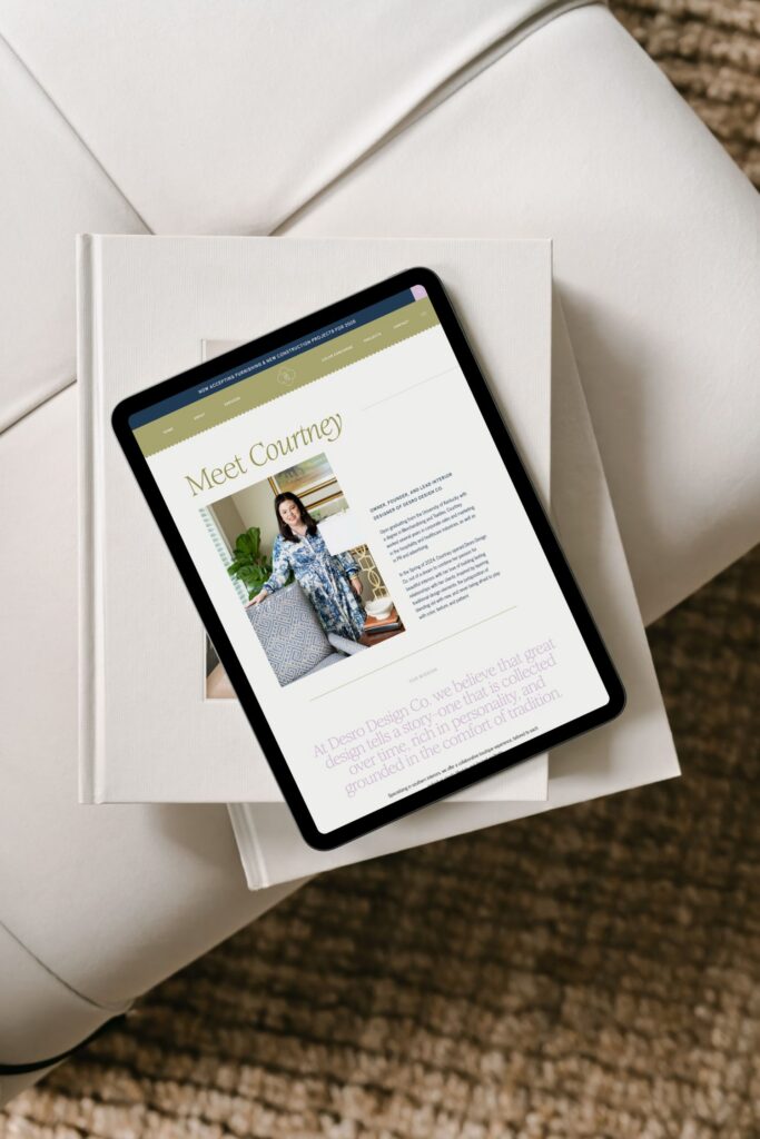 A tablet displaying a website page titled Meet Courtney with a photo of a woman in a blue patterned dress, placed on top of a closed book on a white chair, next to a textured brown rug.