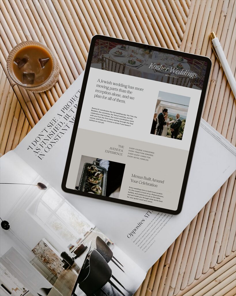 A tablet displaying a webpage titled Kosher Weddings with Avenue K resting on a wooden slatted table next to a glass of iced coffee and an open magazine.
